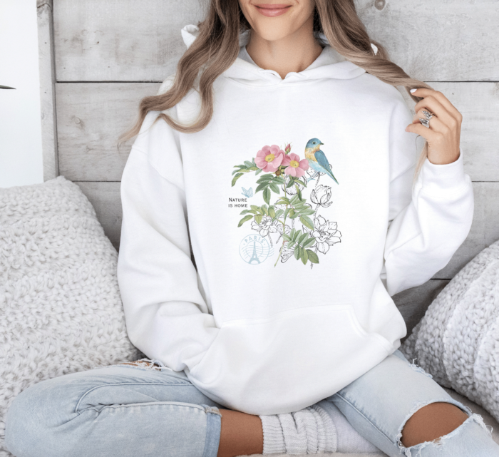 Cottagecore Botanical Bird Hoodie in White, worn by a woman on a soft sofa.