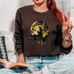 Tuath de danann Dark Academia Chocolate Sweatshirt, With Black Moon Fairy Image worn by girl sitting on a sofa.